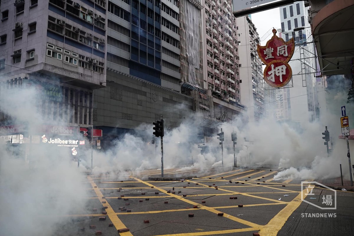 反對「禁蒙面法」的示威者6日下午冒雨兵分多路上街，警方發射催淚彈清場，示威者撐起傘陣掩護撤離。 圖：擷取自立場新聞臉書(資料照片)