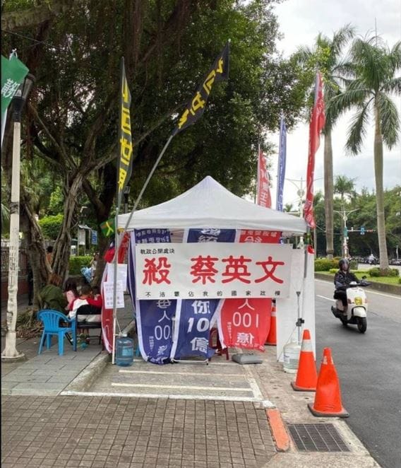 藍信祺在立法院前設置總統連署攤位，並懸掛「殺蔡英文」布條，遭警方帶回偵辦。 圖：翻攝自梁文傑臉書