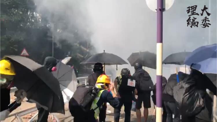 學生以雨傘抵擋警方催淚彈，但擋不住煙霧彌漫。 圖：翻攝自理大學生報編委
