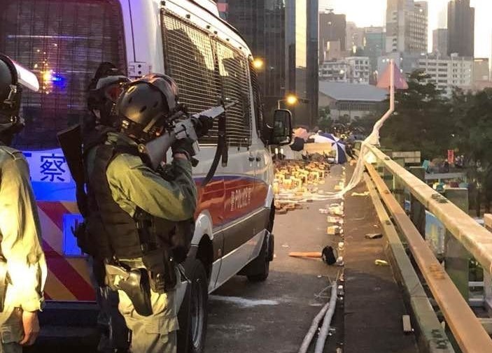 港警躲在車後高舉制暴的「最後武器」AR-15實彈步槍指向理工大學。 圖：翻攝自網路