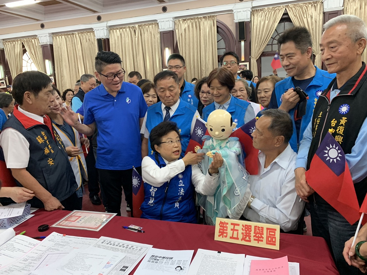「薪傳獎」得主黃文郎，特地帶著精心製作「小韓國瑜布袋戲偶」，陪同沈智慧登記。 圖：沈智慧競選總部/提供