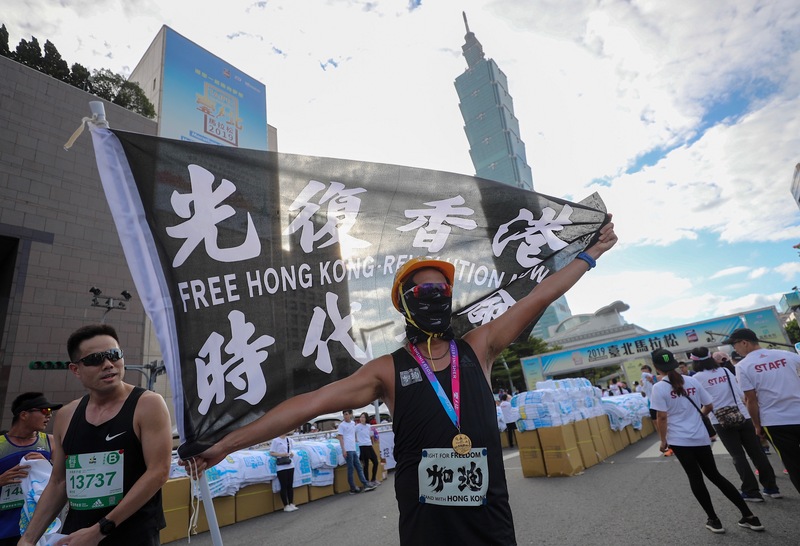 2019台北馬拉松15日在台北市政府前廣場開跑，吸引2萬8000名國內外跑者共襄盛舉，1名跑者完賽後揮舞標語旗幟為香港加油。 圖：中央社提供