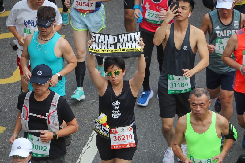2019台北馬拉松15日在台北市政府前廣場開跑，吸引來自62個國家、2萬8000名國內外跑者報名參與，有跑者手舉支持香港標語參賽。 圖：中央社提供