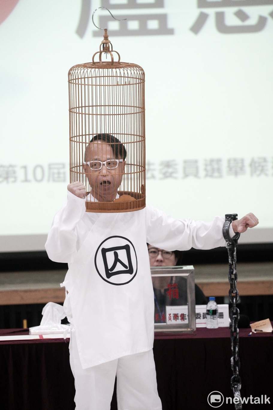 北市選委會今進行區域立委候選人號次抽籤，平常較沒有媒體曝光機會的無黨籍立委候選人盧憲孚用鳥籠罩住自己的頭部，手上還綁著鏈條，在抽完號次後把握機會向媒體發表他的參選理念。 圖：張良一/攝