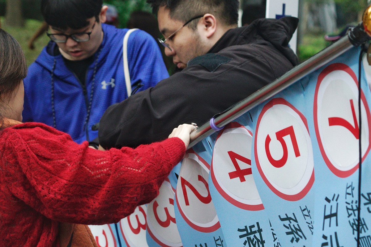 國民黨立委候選人的工作人員在候選人號次抽籤後，立刻將候選人的號次貼在布條上。 圖：張良一/攝