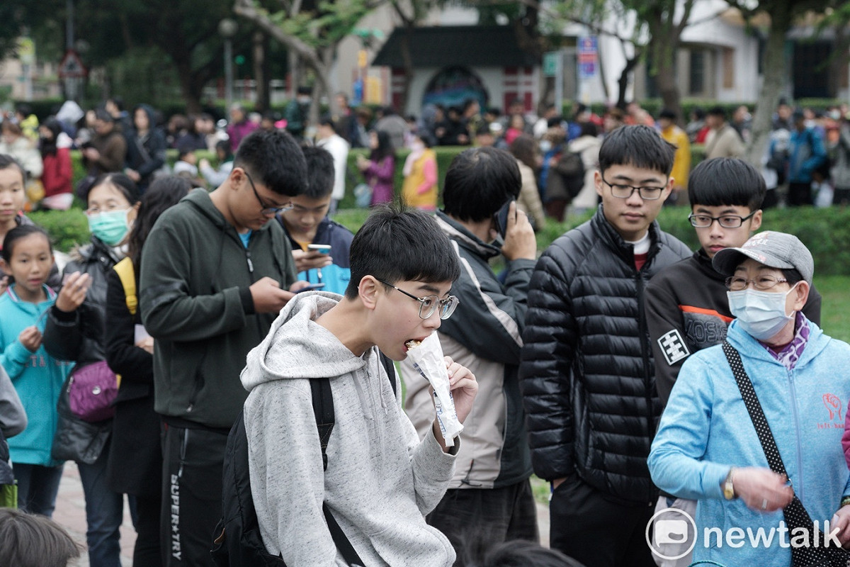 一位年輕人大啖熱騰騰的雞排，還在排隊的一位媽媽問她：「口味如何？好不好吃？」 圖：張良一/攝