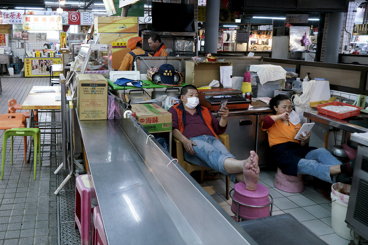 瑞芳美食廣場的攤商利用空檔滑手機。受疫情影響，美食廣場的來客量減少許多。 圖：張良一/攝