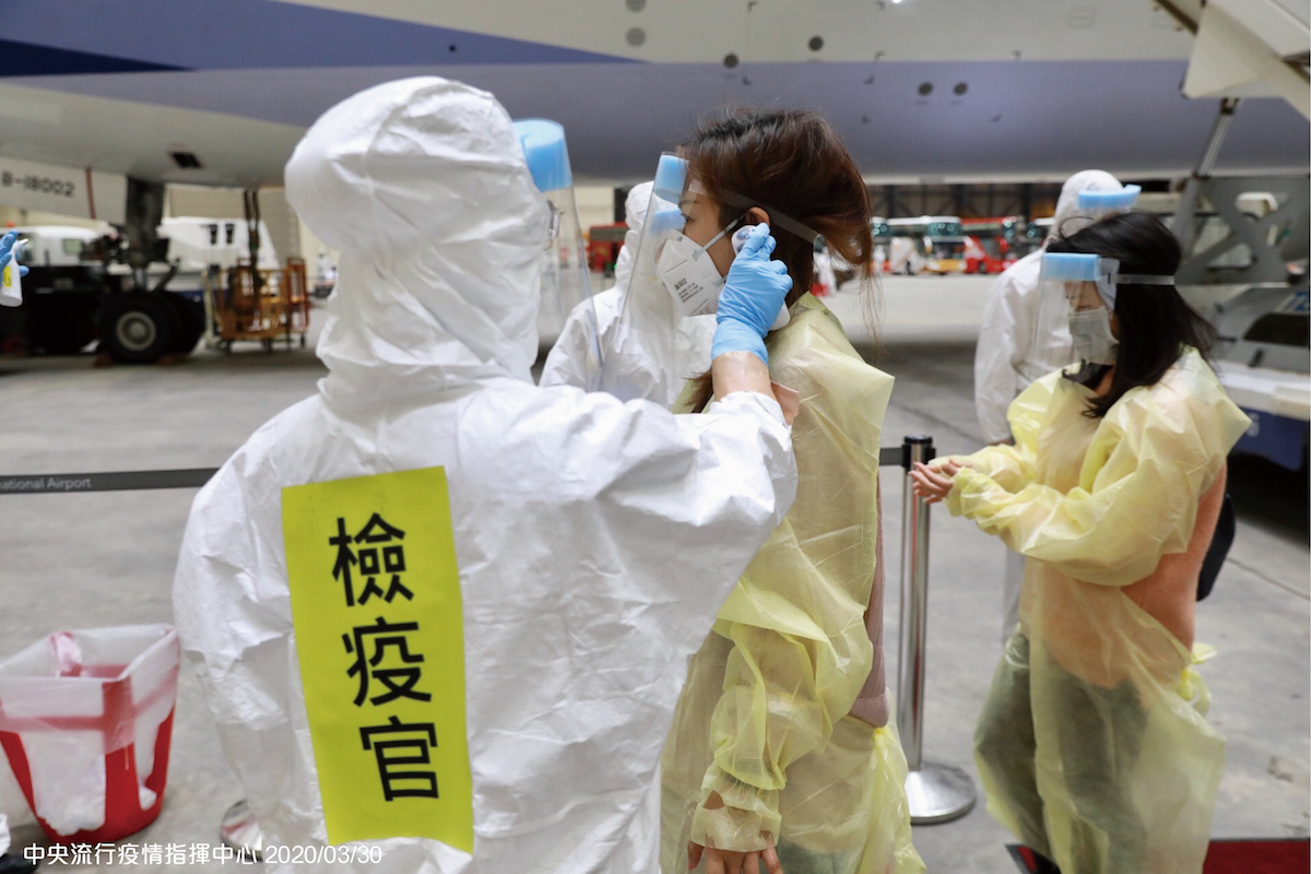 著完整防護裝備的旅客經化學兵一一消毒雙手、鞋子及隨身包包後測量體溫，全程配合現場嚴密之檢疫措施。 圖：中央流行疫情指揮中心／提供