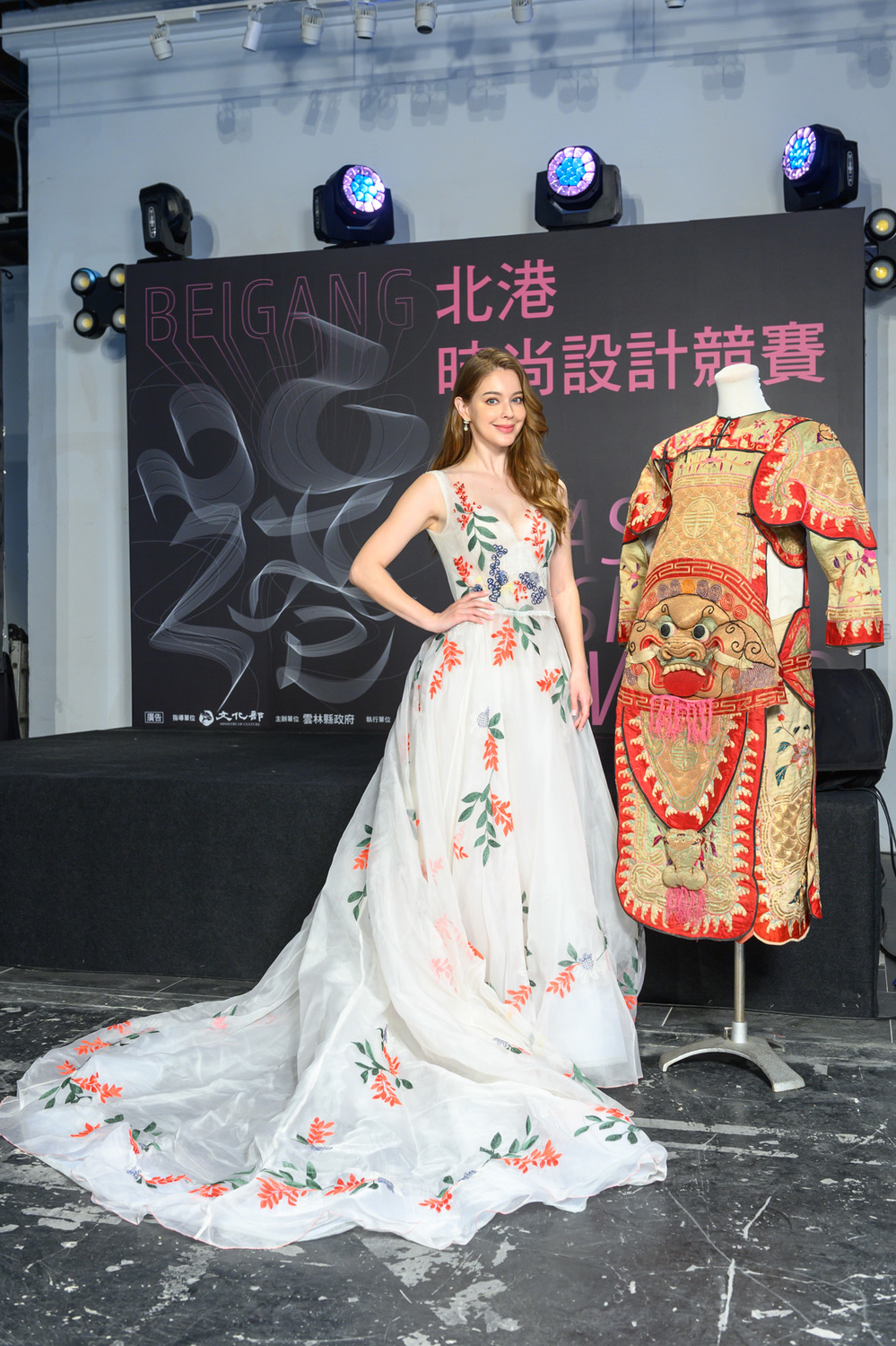 安妮身穿一襲白色刺繡禮服，與集雅軒保存百年戰甲戲服合影。 圖：雲林縣政府文化觀光處/提供