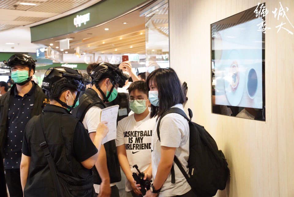 年僅13歲的陸同學與一旁的白衣女記者遭警方圍捕。 圖：翻攝自香港城市大學學生會編輯委員會