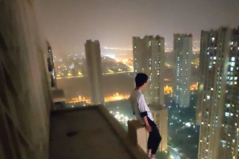 一名青年坐在建築邊緣，並把雙腳懸空在外。 圖：翻攝自新華社微信
