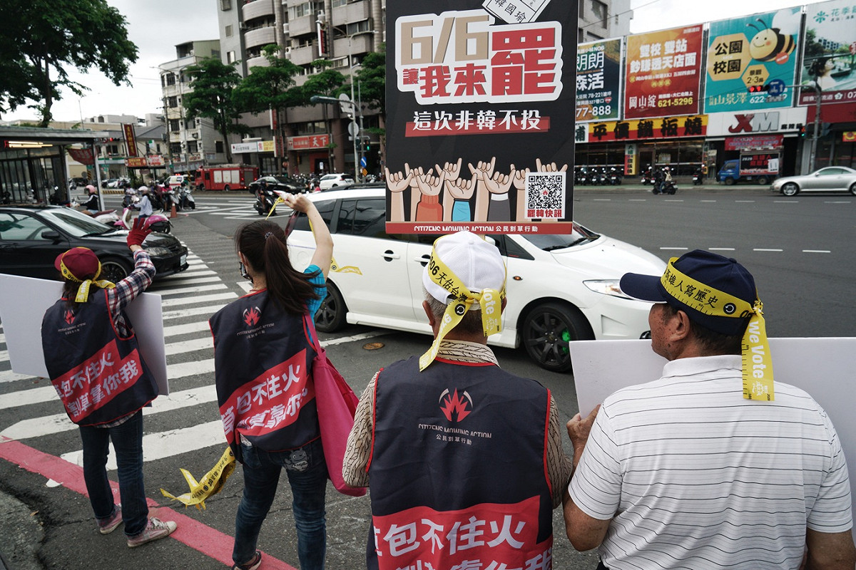 市議員黃秋媖的工作人員在岡山黃昏市場外舉罷韓牌子、發放黃絲帶，為下週末即將登場的罷韓投票，向市民催票。 圖：張良一/攝