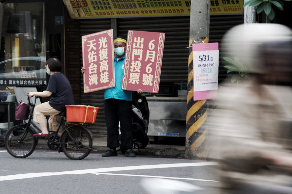 民進黨立委劉世芳的一位工作人員在楠梓火車站前，舉著「6月6號出門投票」、「光復高雄天佑台灣」的牌子，向市民催票。 圖：張良一/攝
