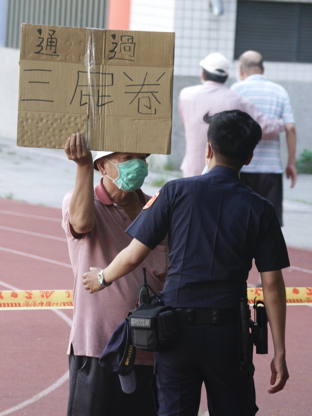 一位民眾在投票所警戒線高舉「通過三屁卷」手舉牌，遭警方前來關切。 圖：張良一/攝