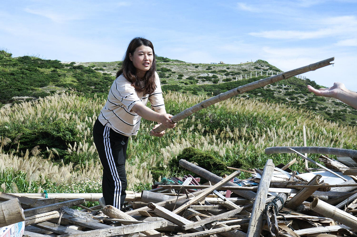 曹芷屏將一根可用的竹竿傳遞給大浦Plus團隊的夥伴，她們在馬祖東莒資源回收場的一堆廢棄物中，尋找可以用來蓋雞舍的素材。 圖：張良一/攝