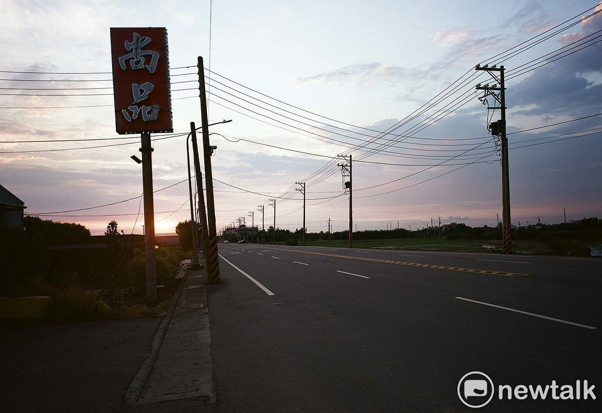 筆直寬闊的四線車道、半空中的廣告看板、電線和電線桿佈滿夕陽餘暉的天際線，空曠的桃園沿海地景中，有著許多不可言說的隱喻。 圖：余白攝影/提供