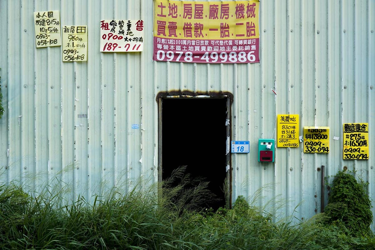 大園區沙崙里的一棟廢棄鐵皮屋，外牆被貼滿了買賣土地的廣告物。 圖：張良一/攝