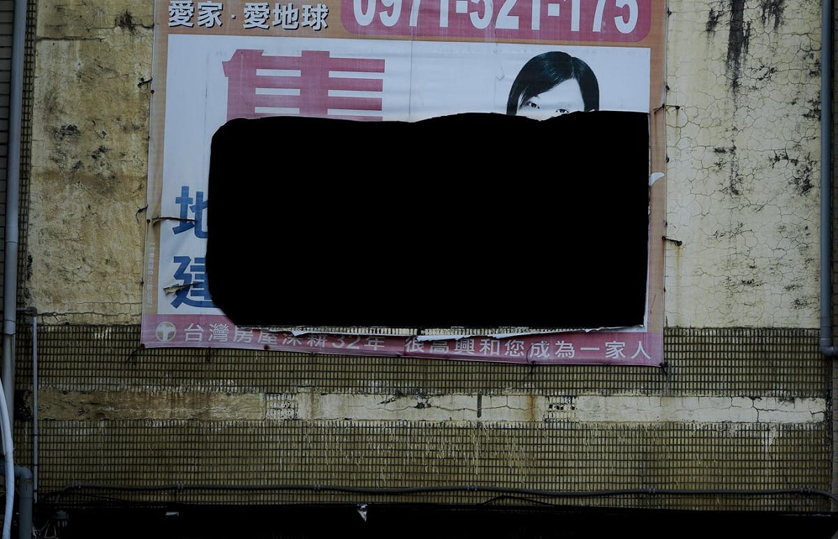 一棟位在桃園蘆竹區的台15線公路上的透天厝，一面房屋買賣的帆布廣告招牌被割了一大洞。 圖：張良一/攝