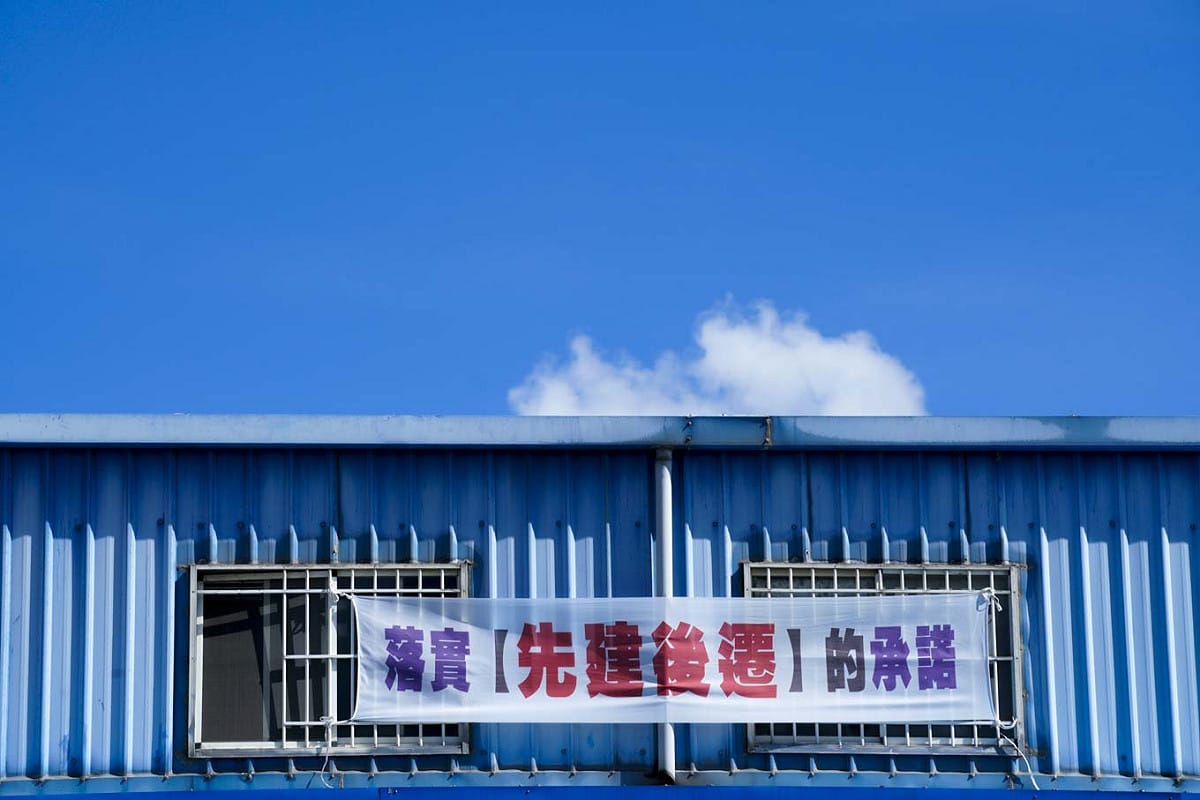 大園區一家汽車修護廠在二樓窗口張貼『落實先建後遷的承諾』的抗議布條。 圖：張良一/攝