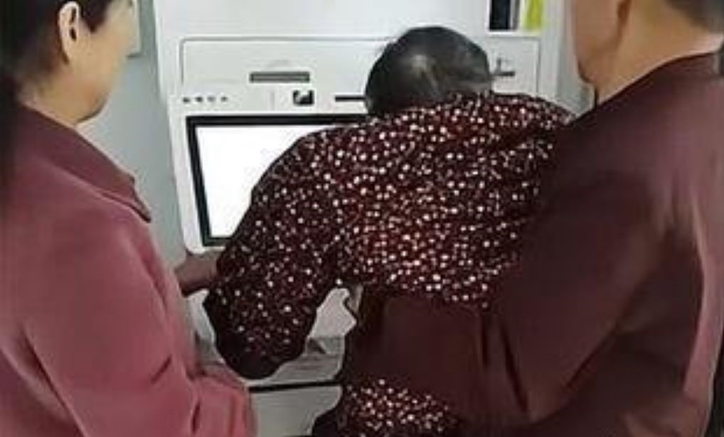 中國湖北廣水一名94歲的老奶奶20日前往銀行辦事，但因為行動不便，靠著親友抱起下才順利完成人臉辨識，而銀行人員見狀並未妥善處理，遭民眾錄影PO在網路上。 圖：翻攝自微博