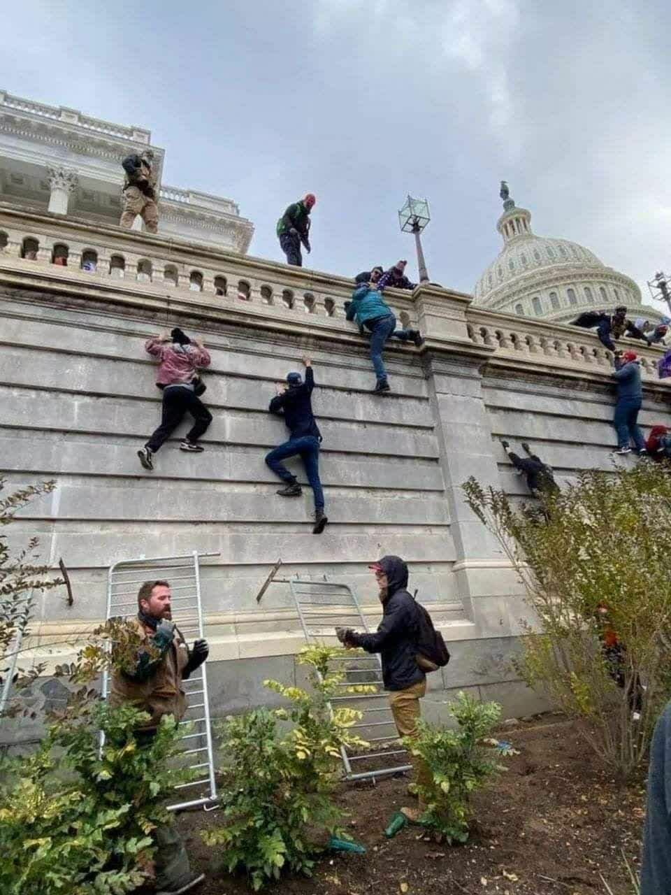 美國暴動民眾爬越國會大樓的高牆，企圖進入議院內。 圖：翻攝自推特