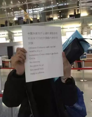 一名中國母親在機場舉牌抗議，牌子上寫著「中國大使館不讓健康報告合格的無家可歸的中國六歲女孩回國」。 圖：翻攝網路