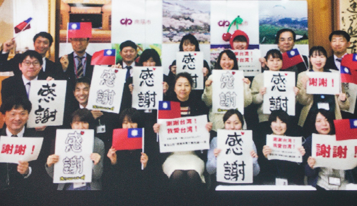 明天就是日本311大地震十週年，台北捷運中山站一號出口目前正以『謝謝台灣！我愛台灣！期待再次相見』為主題的大型海報展覽。現場有1200張日本東北地區的民眾手舉著各種感謝台灣的照片，串聯拼貼成一大片牆面，感謝台灣曾在311大地震大力援助受創的震災災民。圖為東北民眾舉著台灣國旗和『感謝』手舉牌謝謝台灣民眾在日本311大地震的幫忙。 圖：張良一/翻攝