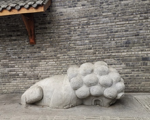 中國街道去年10月出現一尊造型怪異的石獅雕塑，不僅前半截身子陷入地面、後腿彎曲呈蹲狀，一旁也沒有任何標牌能夠解釋其創作意象。 圖：翻攝自微博