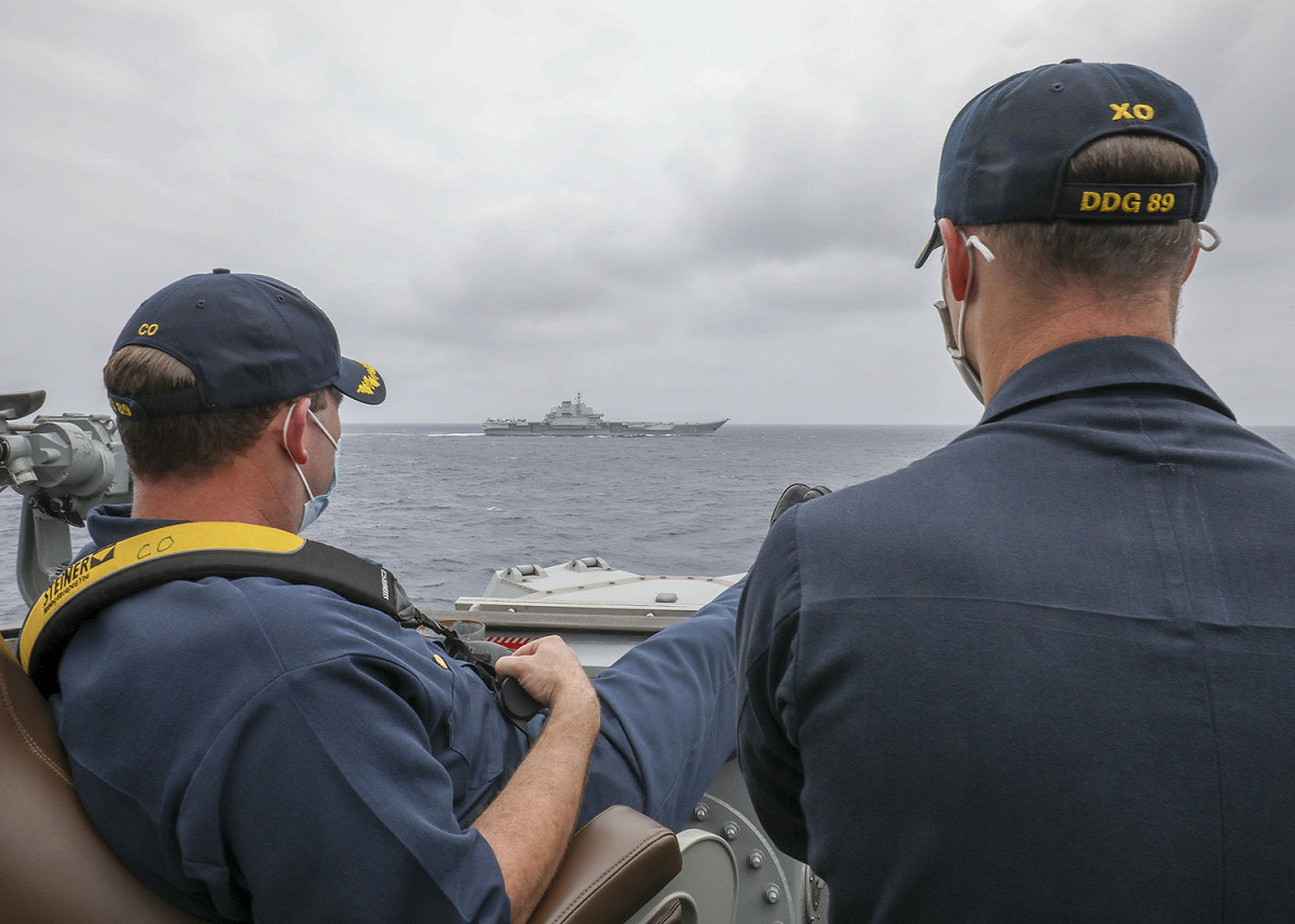 美國海軍日前公布1張馬斯廷號驅逐艦指揮官布里格斯中校（左）翹腳看著中國遼寧艦的照片，他揹的望遠鏡被爆是德國視樂得品牌。 圖：翻攝自美國海軍官網