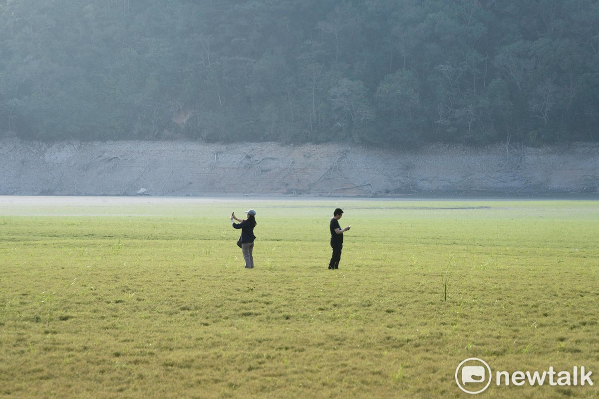 兩位遊客在「日月潭大草原」拍攝水庫乾涸奇景。 圖：張良一/攝