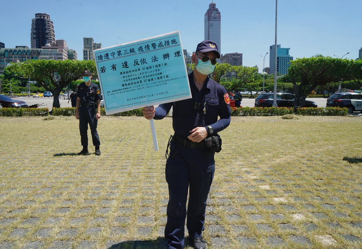 有別於警方經常在抗議現場舉的「行為違法命令解散」手舉牌，今天警方也改用「提醒遵守第三級疫情警戒措施」手舉牌，提醒抗議爭取自身權益的同時，也不要違反防疫規定。 圖：張良一/攝