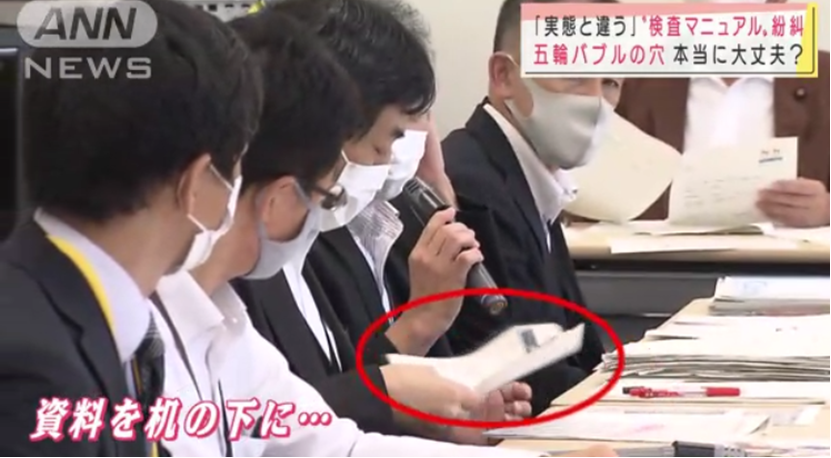 東京奧運會官員把桌上打印出來的工作指南往桌子底下藏。 圖 : 翻攝自朝日電視台畫面