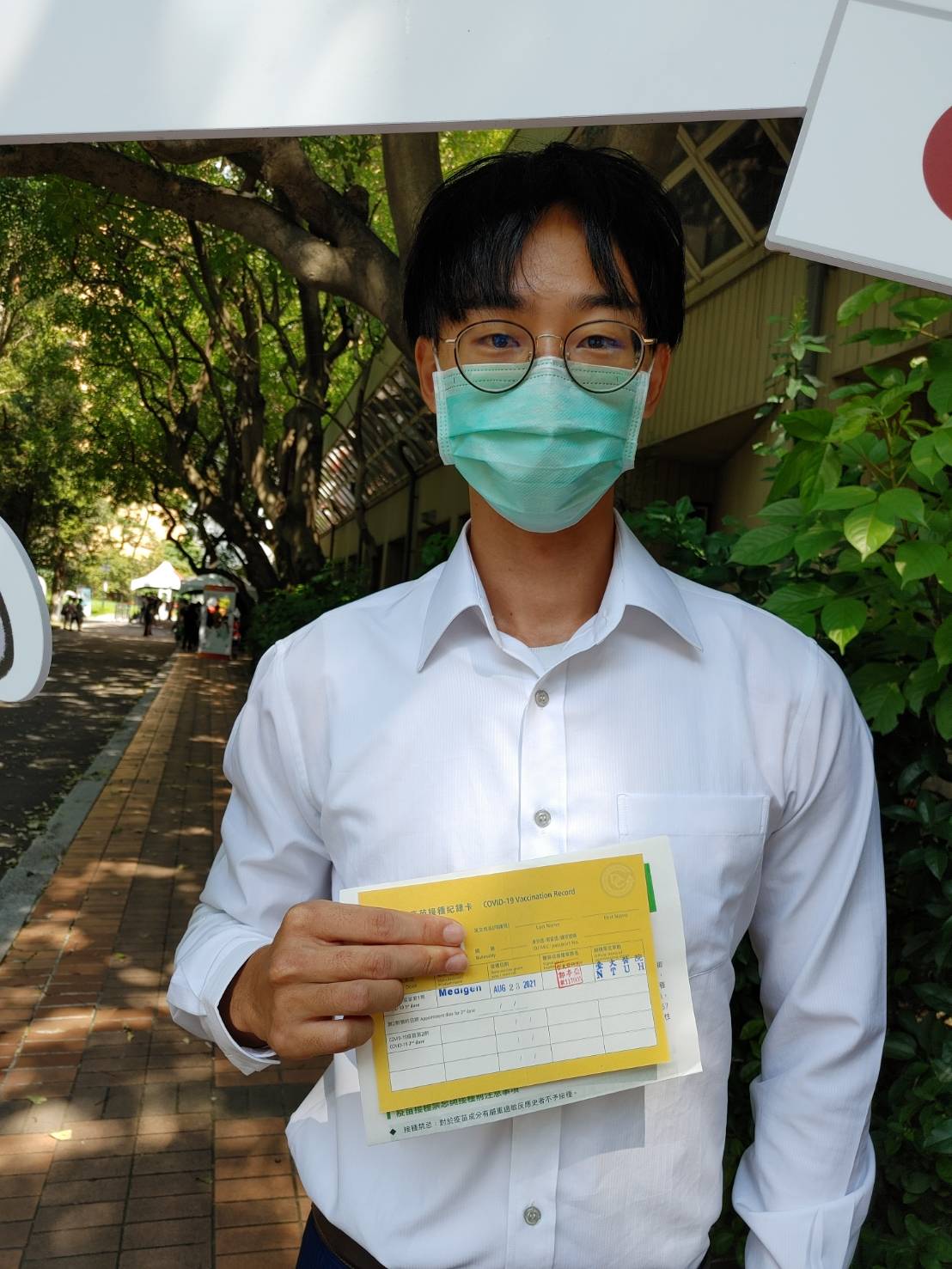 開心拿著疫苗接種卡在台大醫院安排的打卡區拍照留念，他呼籲所有跟他一樣的年輕人，應該踴躍接種疫苗。 圖／新頭殼
