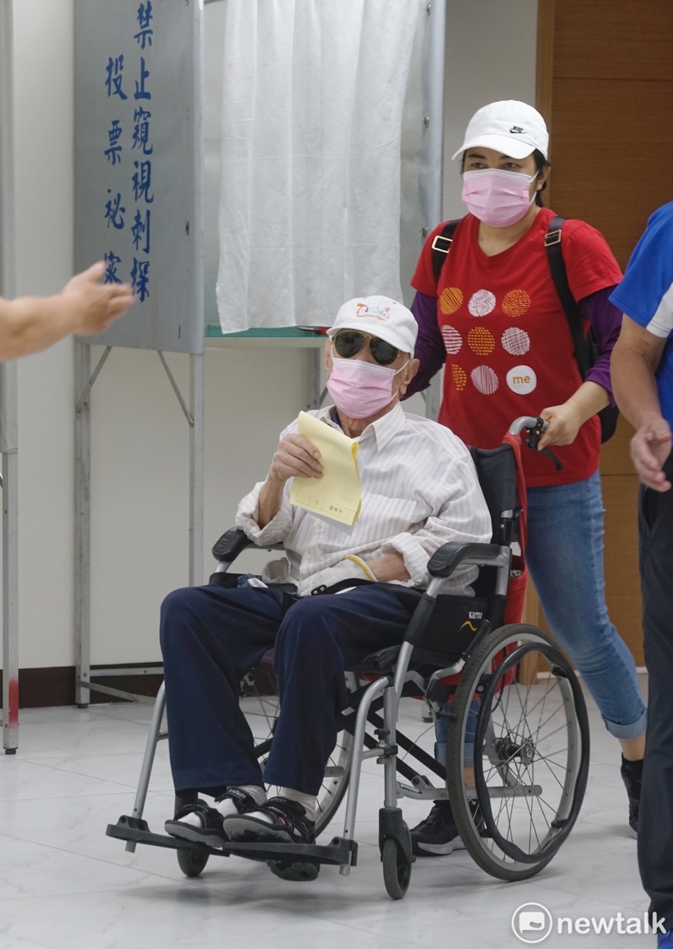 一位老黨員坐著輪椅，並在外籍移工的協助下投票。 圖：張良一/攝