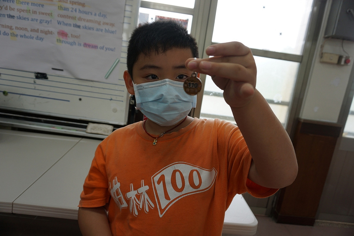 小學生手上拿的是今年度狂犬病疫苗注射證明金色頸牌。 圖：新北市動保處提供