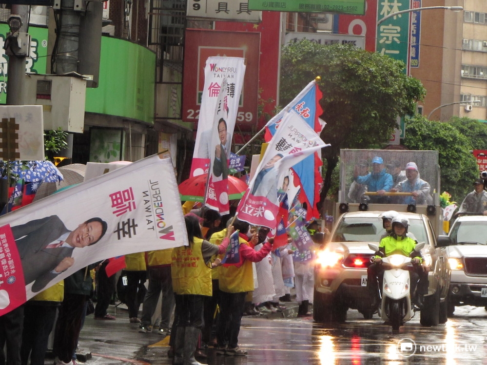 國民黨主席朱立倫6日上午陪新北立委候選人張慶忠、林德福、羅明才掃街拜票，沿途可見民眾在雨中伸長脖子、搖旗歡迎。 圖：邱珮文/攝