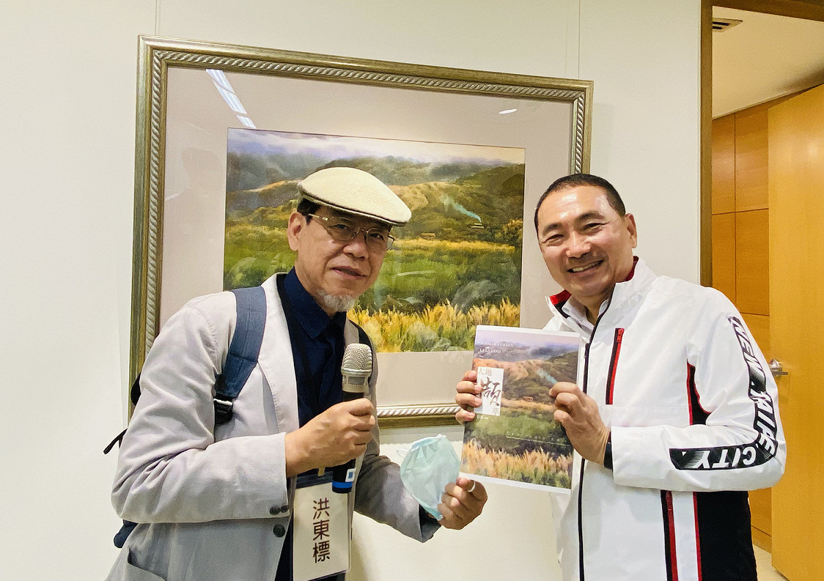 藝術家洪東標（左）與侯友宜（右）手持藝術家《大地擷萃》書籍，一同於作品《大屯向晚》前合影。 圖：新北市文化局提供