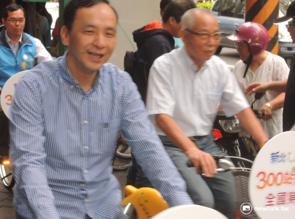 有位女性民眾的機車停放在新北市長朱立倫騎乘YouBike動線中，但機車一時發不動而遭工作人員的催趕，朱立倫一行人則神情自若的從一旁騎YouBike抵達會場。 圖：陳冠廷/攝