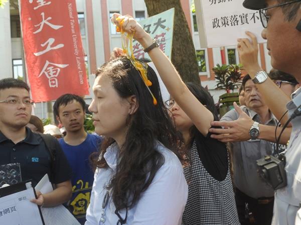 數十名學生代表4日在教育部大門口，舉行「反對大學假學習真勞動」聯合行動記者會，1名學生在出面接受陳情的教育部高教司專委王淑娟（中）頭上捏爆生雞蛋。 圖：中央社