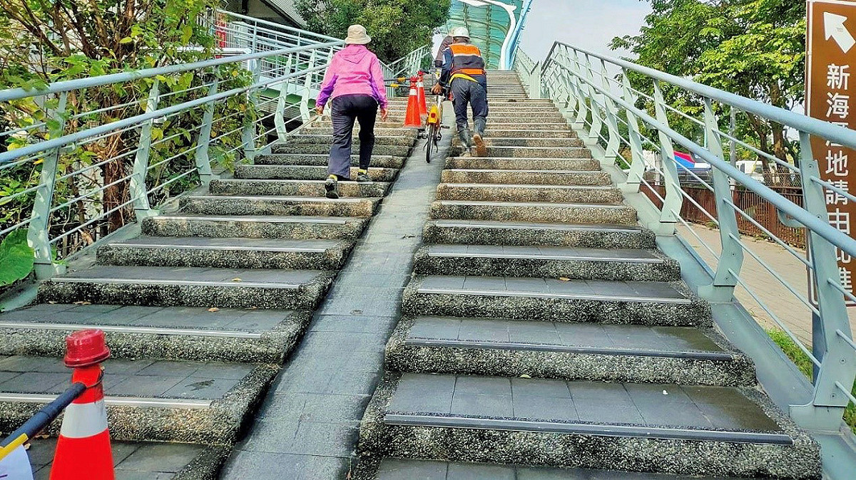 新北市雙溪口陸橋施工人員協助民眾，牽引自行車至河濱公園。 圖：新北市水利局/提供