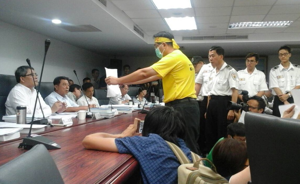 內政部都委會9日開會審議南鐵案，反南鐵東移自救會成員9日出示手牌陳情時，重重警力站在主席台前戒護。 圖：水資源保育聯盟提供