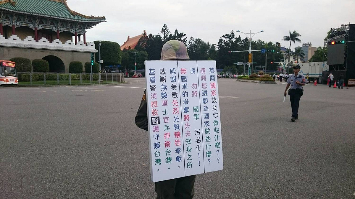 這位穿著軍服參與93大遊行的民眾，只要看到有人拿相機拍攝，就立刻舉起海報遮住臉部。 圖：林朝億/攝