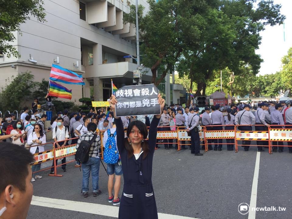到立法院現場為同性婚姻發聲的跨性別女生，被警察團團包圍，仍高舉「歧視會殺人，你們都是兇手」標語。 圖：柯昱安/攝