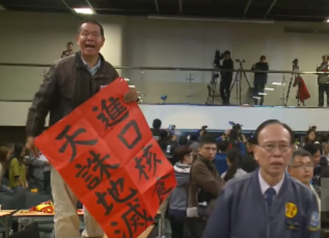 25日舉行的核食公聽會，在藍軍各團體動員下，再度混亂收場，圖為民眾激動跳上公聽會現場桌子抗議。 圖：翻攝日本食品輸台公聽會直播畫面