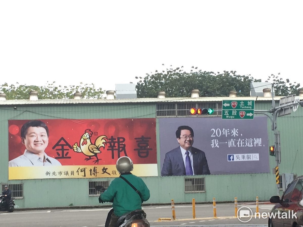 最有玄外之音的莫過於這兩面，矗立在板橋環河路的新莊五股選出的吳秉叡戶外看板，斗大的字是「20年來，我一直在這裡」、並排而立的是，新北市議員何博文的金雞賀歲戶外看板， 圖: 羅碧霞/攝