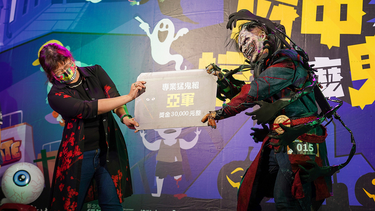 萬聖節變裝比賽鬼怪組的亞軍是「他很奇yeeeeeeeee」，驚悚程度爆表，由經發局長何怡明（左）頒獎。 圖：新北市經發局提供