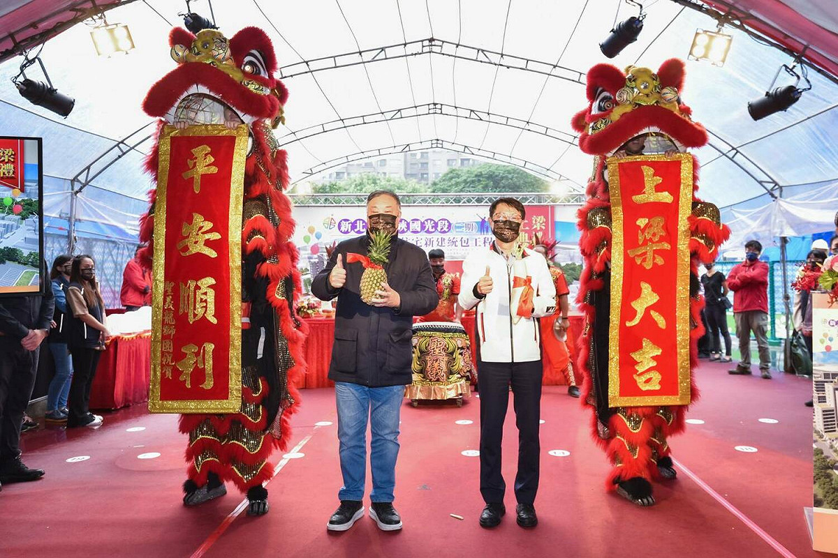 皇昌營造董事長江程金與新北市副市長陳純敬手持鳳梨及菜頭，象徵「旺來」、「好彩頭」。 圖：新北市城鄉局提供