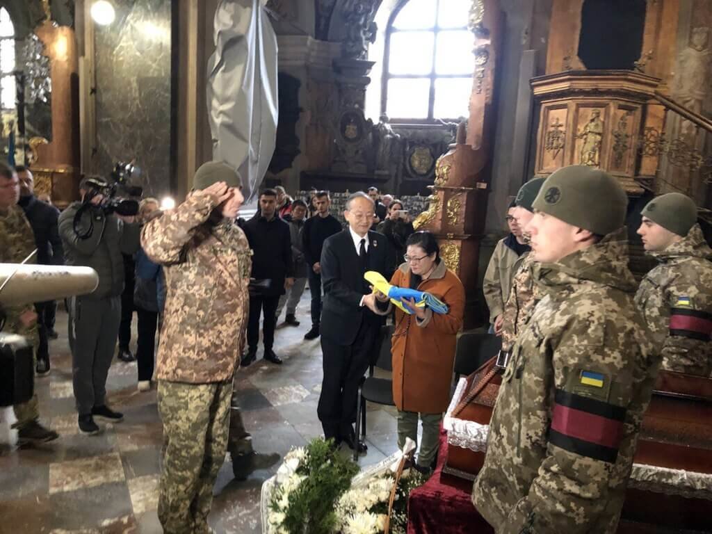 烏克蘭軍方舉辦曾聖光追思儀式，軍方代表向曾聖光致敬，駐波蘭代表陳龍錦（黑色西裝者）陪同家屬。 圖：外交部提供