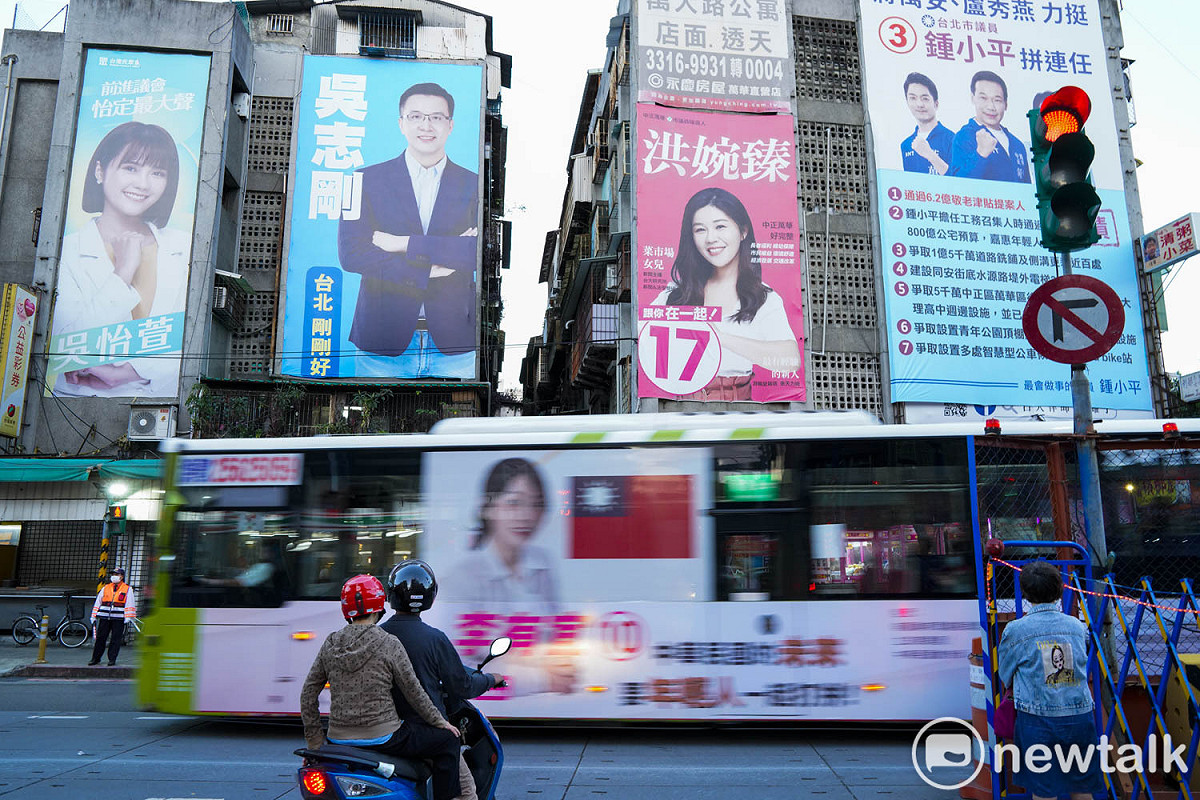 北市萬華區萬大路上一棟公寓外牆貼滿了候選人的競選看板，連經過的公車也貼滿候選人的廣告看板。 圖：張良一/攝