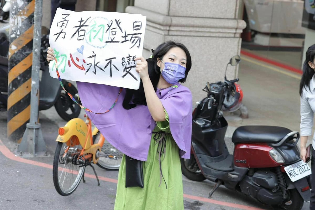 1名可愛的粉絲披著鄭運鵬的紫色斗篷，肩上立著1隻乖巧黑貓，努力騎YouBike趕上車隊，就為了秀出「勇者初登場 初心永不變」的自製標語牌，笑容融化網友。 圖：翻攝自鄭運鵬 Cheng Yun-Peng臉書